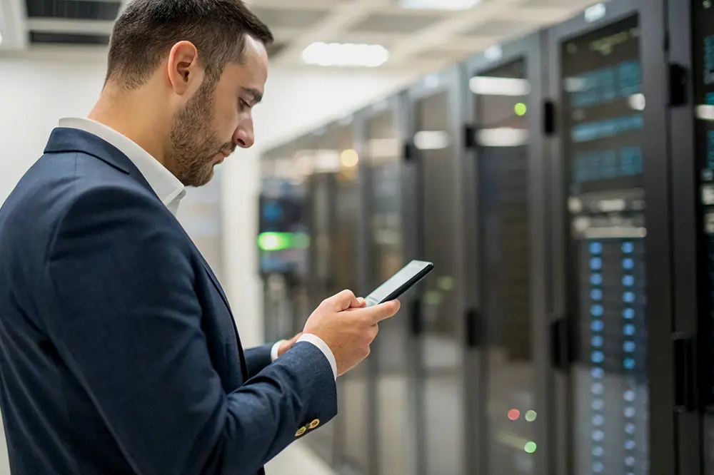 Mann im Anzug prüft sein Smartphone zwischen Serverschränken