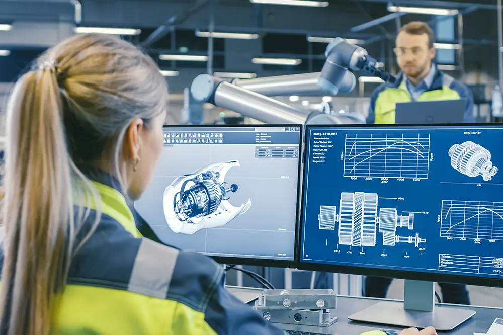 Ingenieurin arbeitet an CAD-Zeichnungen auf zwei Monitoren in einer Werkhalle