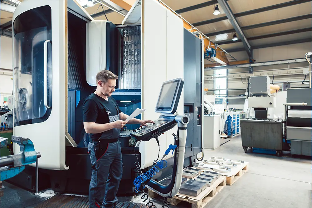 Maschinenbediener am Steuerpult einer CNC-Maschine in einer Werkhalle