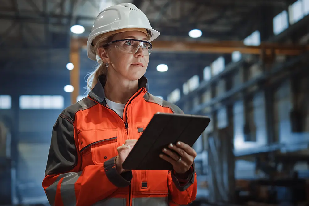 Technikerin mit Schutzhelm und Tablet in einer Industriehalle