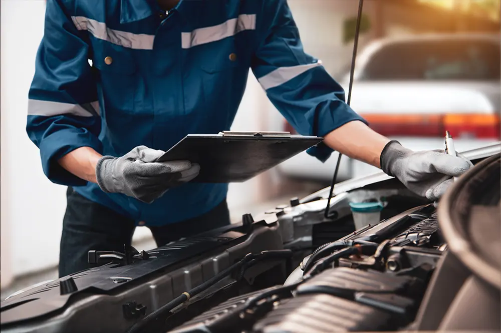 Servicetechniker mit Klemmbrett am geöffneten Motorraum eines Fahrzeugs